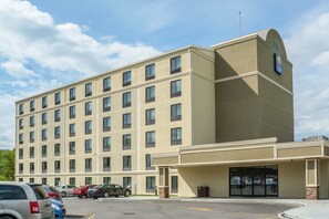 A multi-story hotel with a beige facade, a large entrance with a glass door, and a parking lot with several cars. - Comfort Inn The Pointe (Niagara Falls)