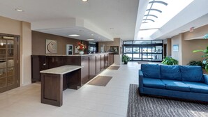 Un vestíbulo de hotel con mostrador de recepción, un sofá azul y un amplio ventanal que proporciona luz natural.