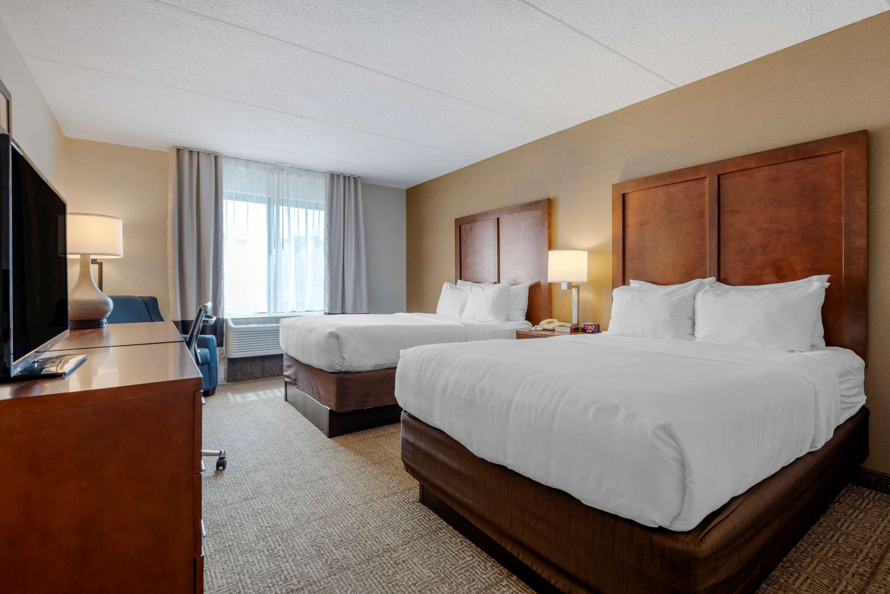 A hotel room with two beds, a desk, a chair, and a TV.