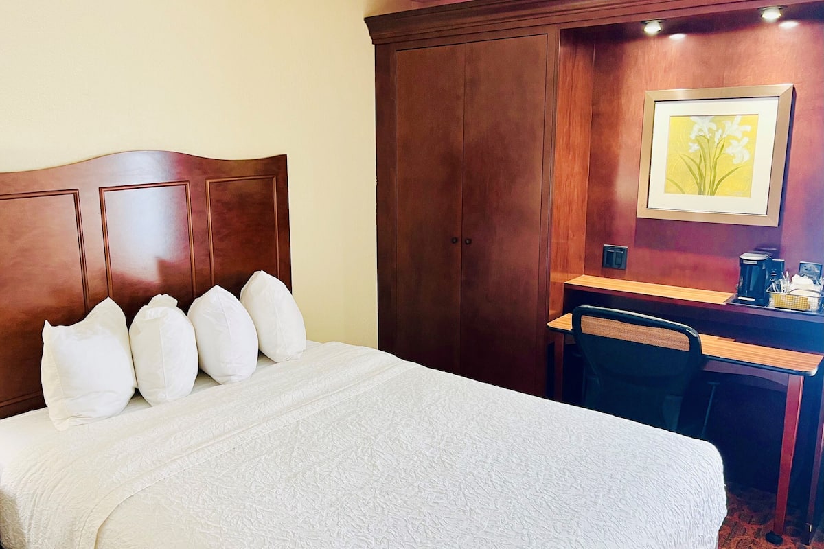 A hotel room with a large bed, a wooden desk, a chair, and a framed picture on the wall.