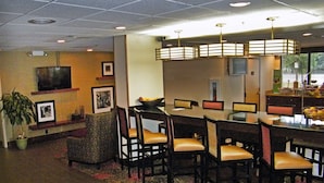 A hotel dining area with a long table, multiple chairs, a television, framed pictures, and a potted plant. - Hampton Inn Norfolk/Chesapeake (Greenbrier Area) (Chesapeake)