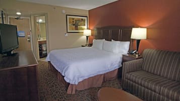 A hotel room with a large bed, two bedside lamps, a television, a sofa, and a desk.