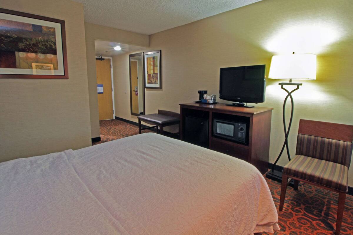 A hotel room with a bed, a television on a stand, a desk with a chair, and a lamp.
