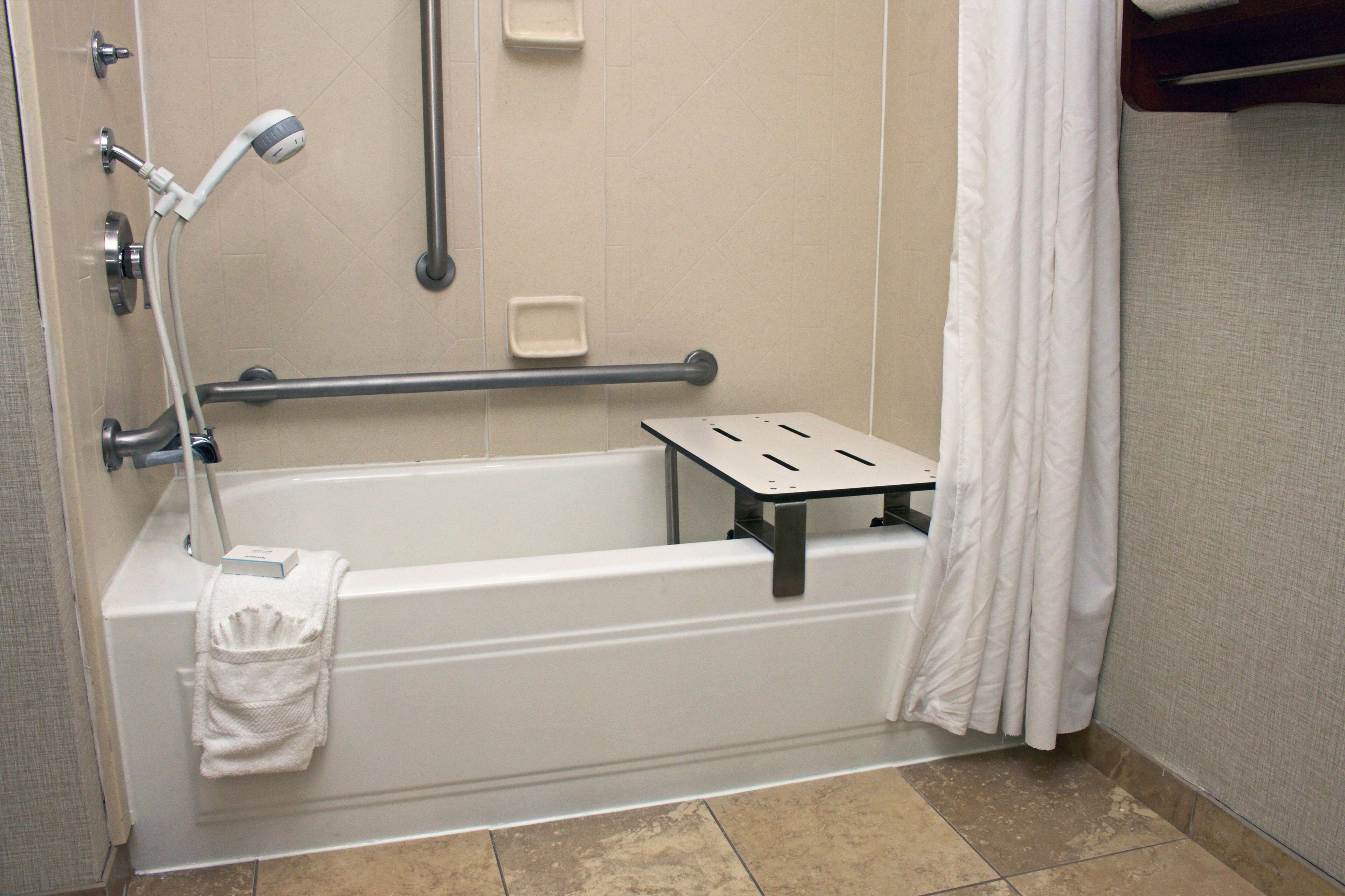 Un baño de hotel estándar con bañera, ducha y barra de apoyo.