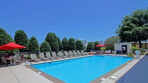 A rectangular swimming pool with a clear blue water, surrounded by lounge chairs and red umbrellas. - Hampton Inn Norfolk/Chesapeake (Greenbrier Area) (Chesapeake)