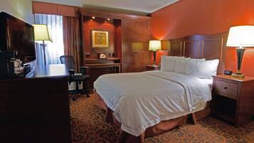 A hotel room with a bed, desk, chair, and lamps.