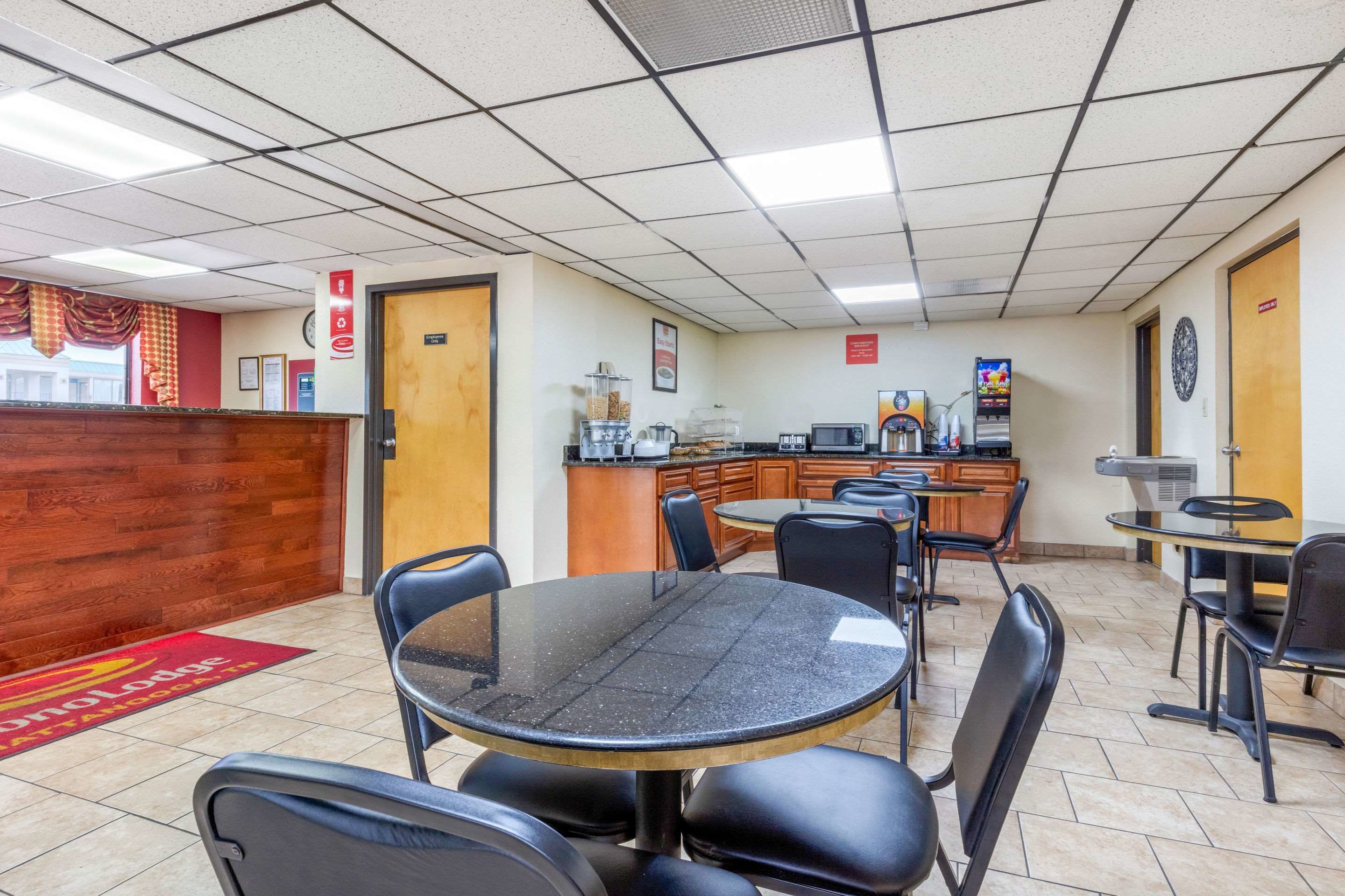 A restaurant with a wooden reception desk, multiple tables and chairs, a kitchen area, and a tiled ceiling.