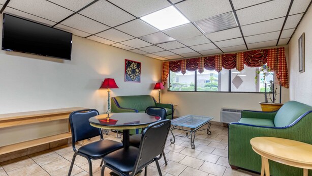 A hotel room with a flat-screen TV, a green sofa, a small round table, and two chairs. - Econo Lodge Chattanooga Northeast - Ooltewah (Chattanooga)