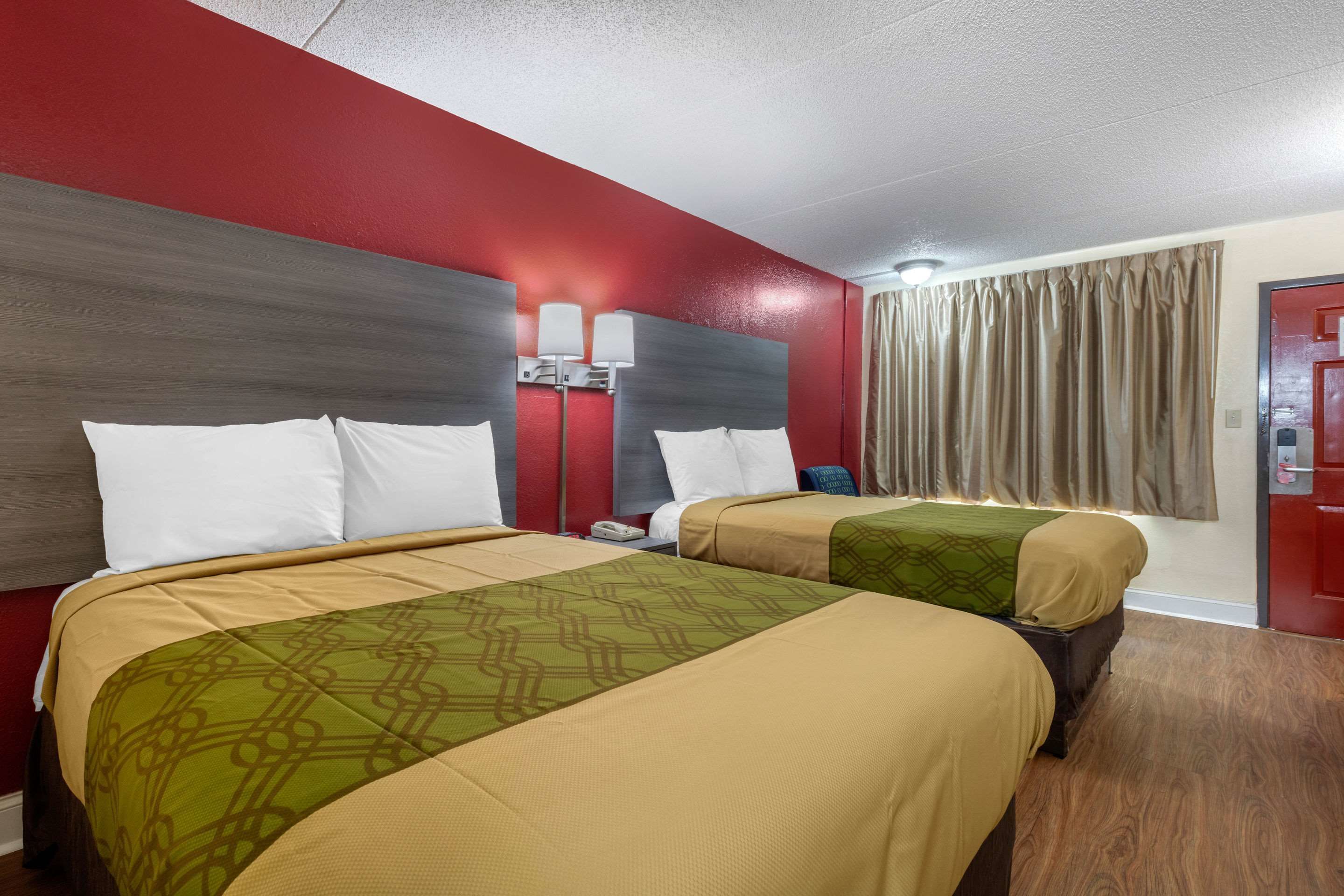 A hotel room with two beds, red walls, a wooden floor, and a red door.