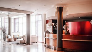 Un área de recepción moderna con un mostrador de madera, una planta grande en maceta y una sala de estar con sofás y una mesa de centro.