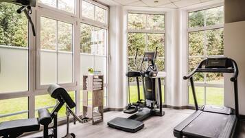 Un gimnasio en casa con equipo de ejercicio, ventanas amplias y vistas a zonas verdes.