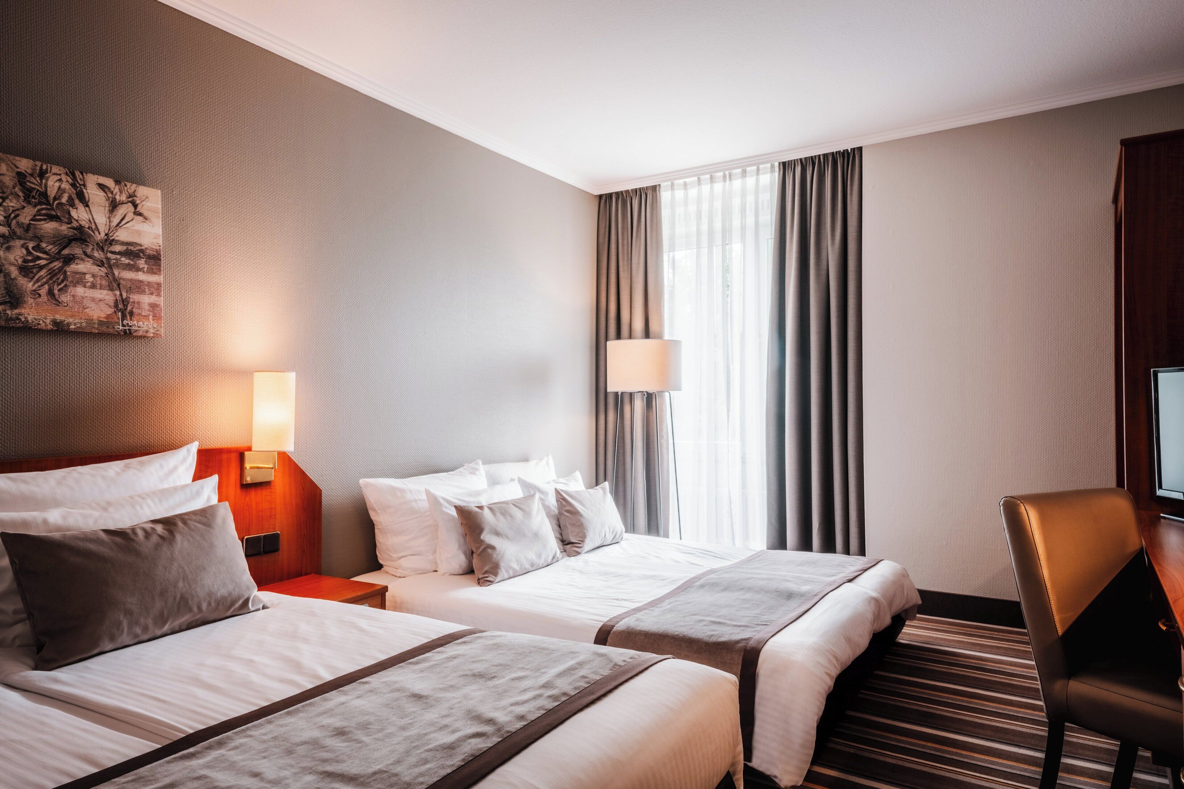 Ein Hotelzimmer mit zwei Betten, einem Schreibtisch, einem Stuhl, einer Lampe und einem Bild an der Wand.