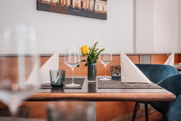 Une table à manger dressée avec des verres transparents, un vase contenant une fleur jaune et une serviette.