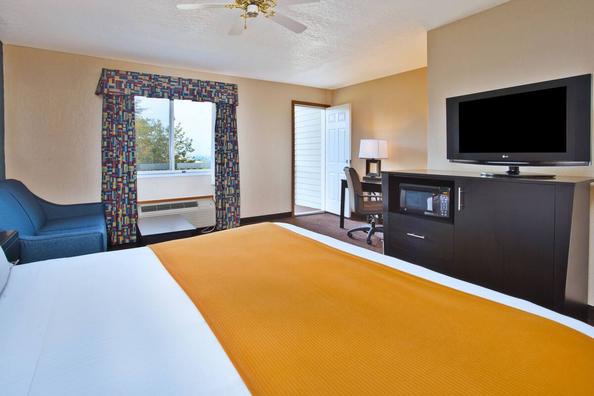 Habitación de hotel con cama, escritorio, computadora, televisión y ventana con cortinas.