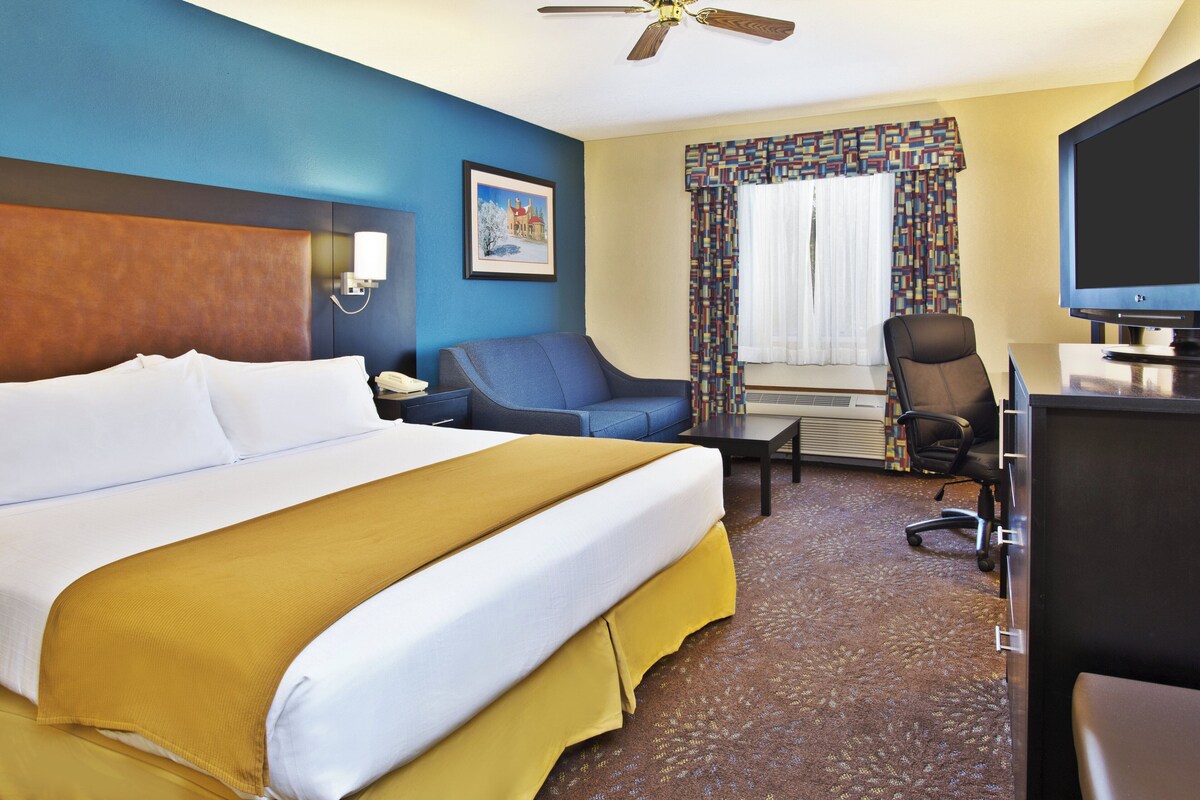 A hotel room with a large bed, a desk, a chair, a television, and a ceiling fan.