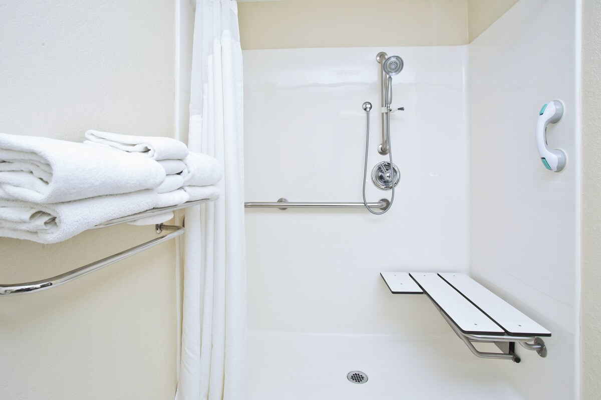 A shower with a handheld showerhead, a grab bar, and a towel rack with folded towels.