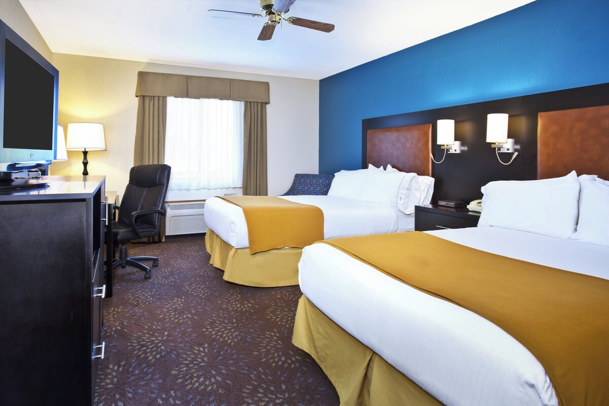 A hotel room with two beds, a desk with a computer, a chair, a television, and a ceiling fan.