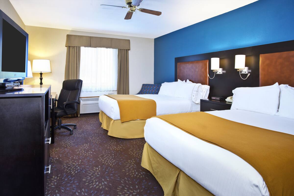 Habitación de hotel con dos camas, un escritorio con computadora, una silla, un televisor y un ventilador de techo.