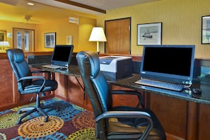 Una habitación de hotel con un escritorio, dos sillas, una impresora y una computadora.