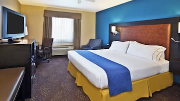 Hotellihuone, jossa on sänky, työpöytä, tuoli, televisio ja kattotuuletin.