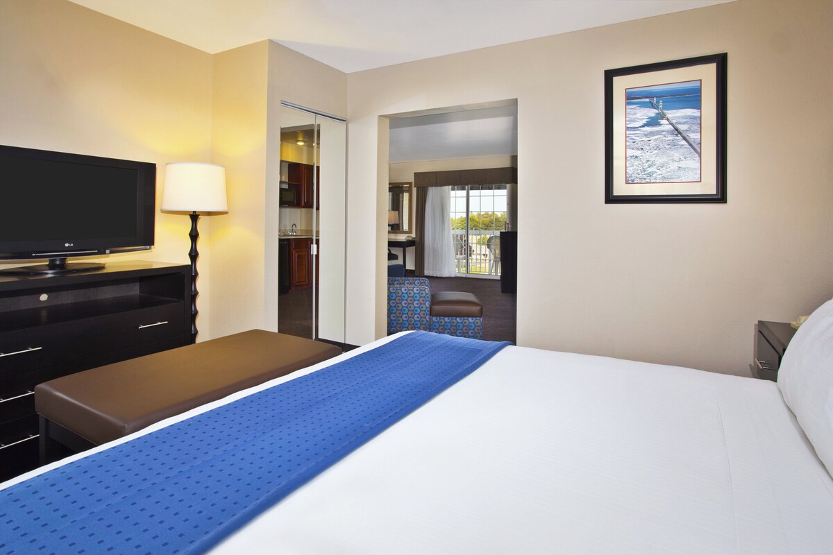 A hotel room with a bed, a TV, a desk, and a bathroom visible through an open door.