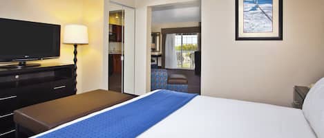 A hotel room with a bed, a TV, a desk, and a bathroom visible through an open door.