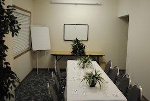 Una sala de conferencias con una larga mesa, sillas, una pizarra y plantas en macetas.