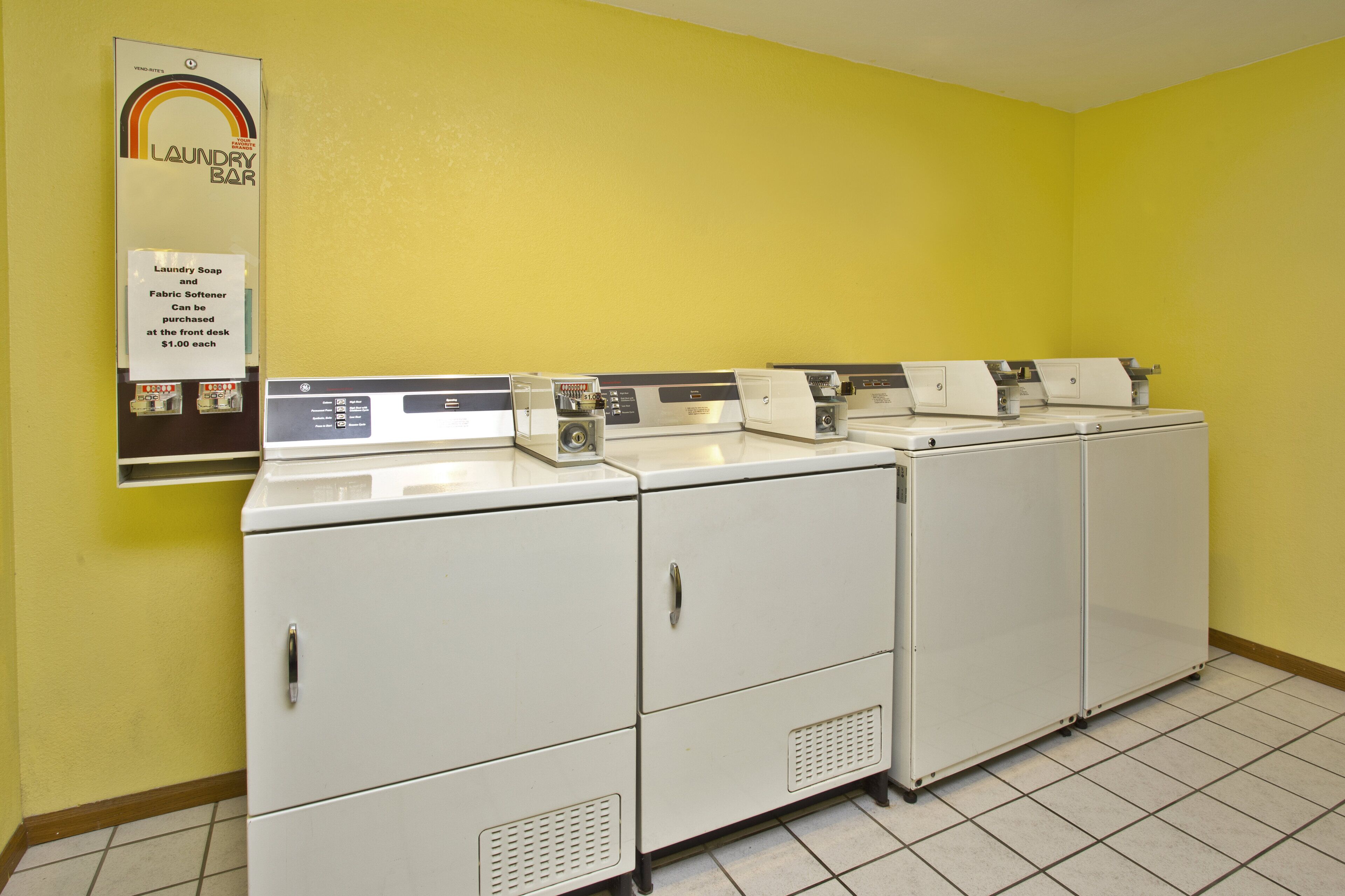 A laundry facility with multiple washing machines and a sign indicating the availability of laundry soap and fabric softener for purchase.