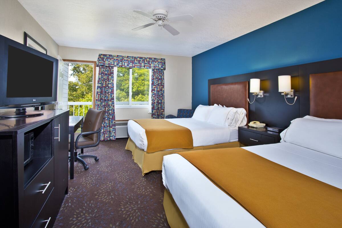 A hotel room with two beds, a desk with a TV, a chair, and a window with curtains.