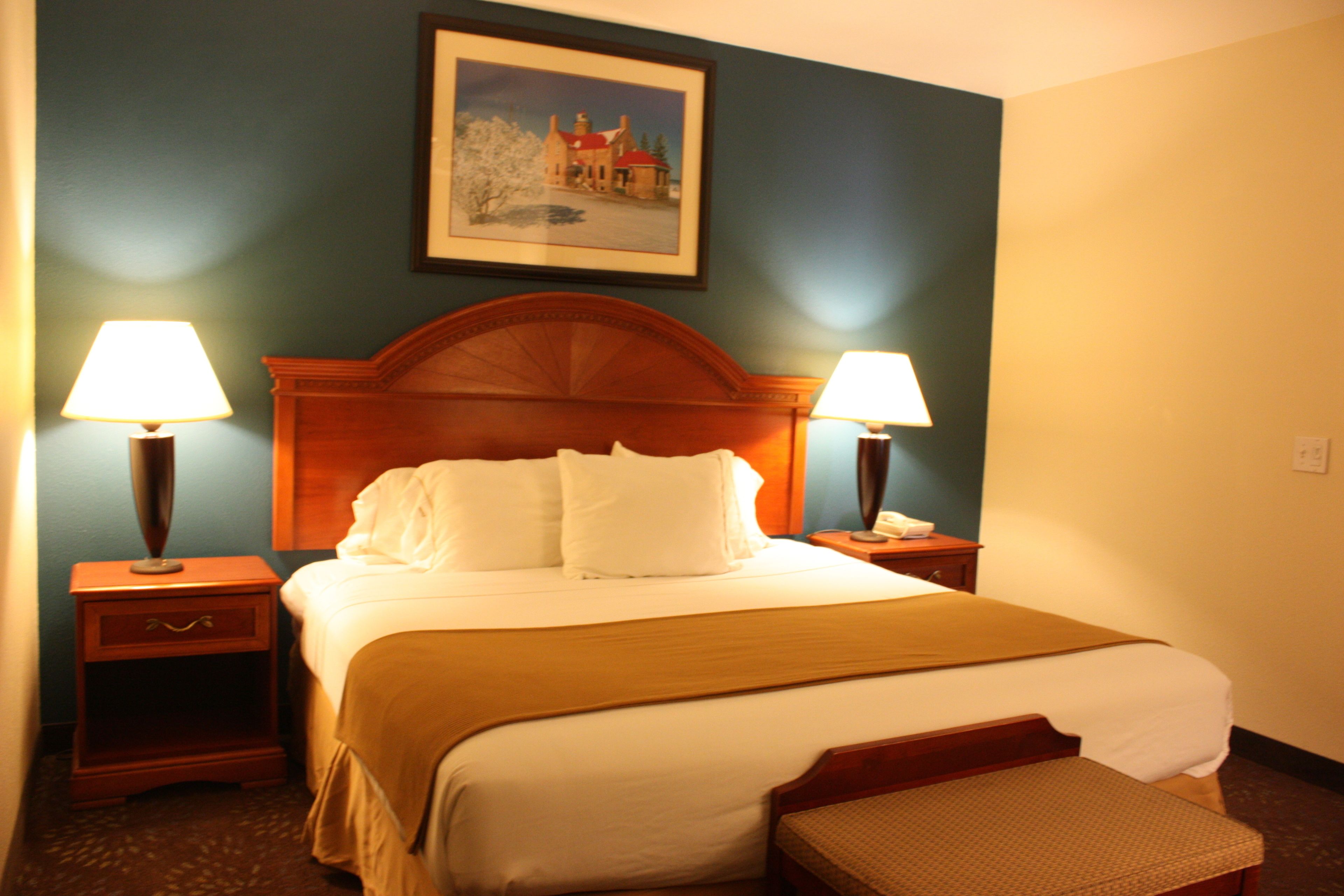 A hotel room with a large bed, two bedside lamps, a wooden headboard, a bench, and a framed picture on the wall.
