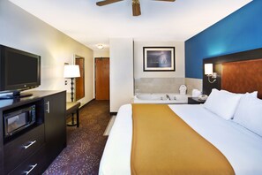A hotel room with a bed, a television, a microwave, a bench, a bathroom with a bathtub, and a ceiling fan. - Holiday Inn Express Mackinaw City by IHG (Mackinaw City)