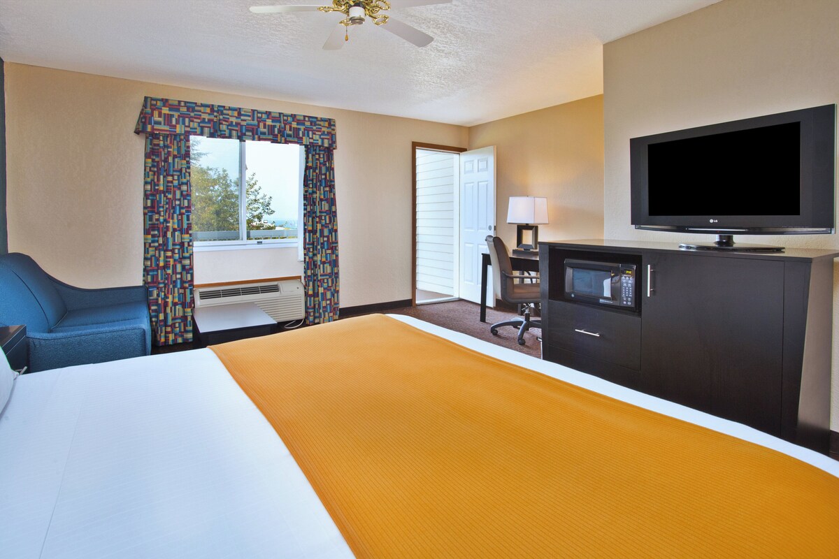 A hotel room with a bed, a television, a desk with a lamp, and a window with curtains.