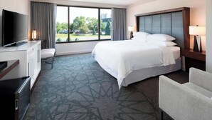 Habitación de hotel con cama, escritorio con televisor, una silla y ventana con cortinas.