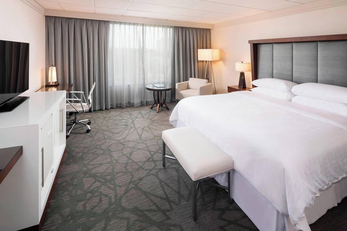 Habitación de hotel con una cama grande, un escritorio, una silla, una mesita y un televisor.