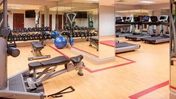A gym with exercise equipment, treadmills, and a mirrored wall.