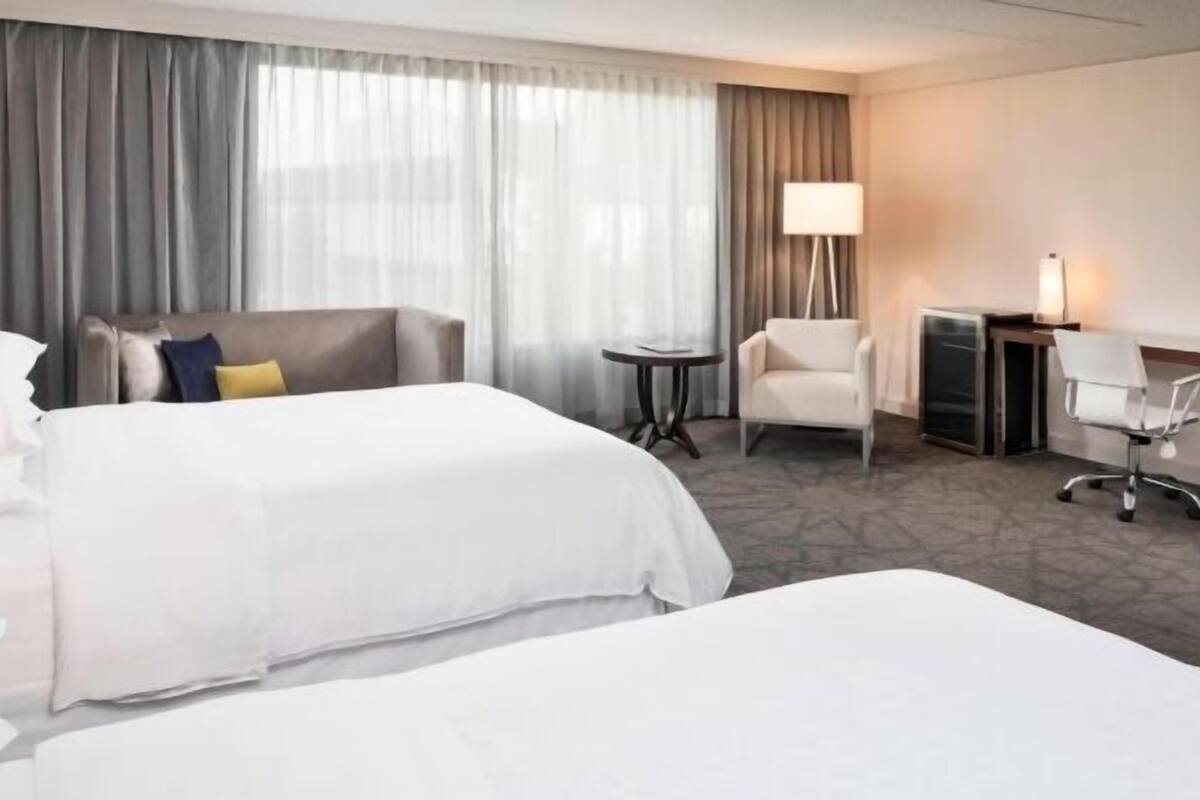 Habitación de hotel con dos camas, un escritorio, una silla y una lámpara.