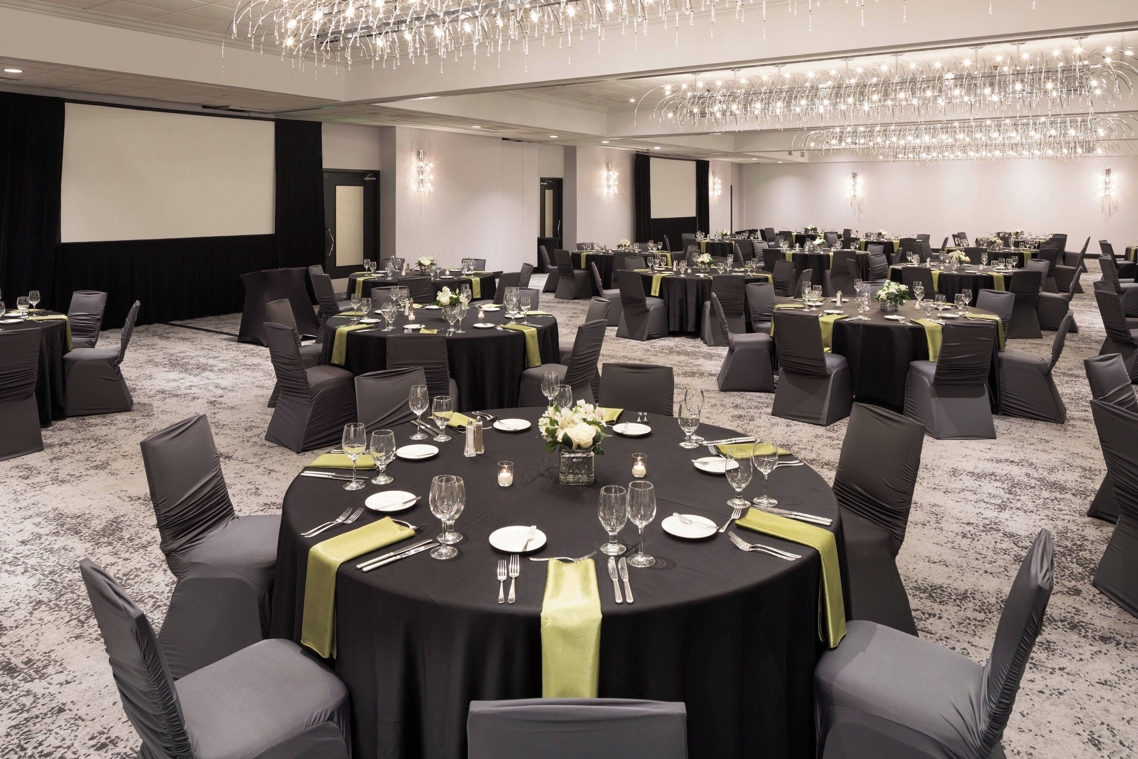 A conference room with multiple round tables, each set with chairs, plates, cutlery, and glasses.