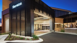 Un hotel Sheraton con fachada moderna, amplio acceso de vidrio y un área exterior bien cuidada con plantas.