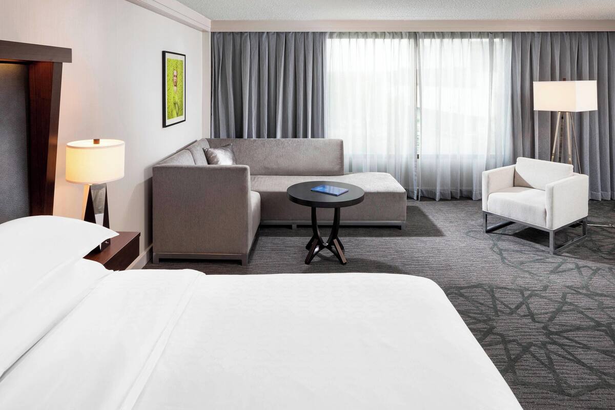 Una habitación de hotel con una cama grande, un sofá, una silla, una mesita redonda y una lámpara.