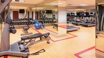 Un gimnasio con máquinas de cardio, bancos de pesas y pelotas de ejercicio.
