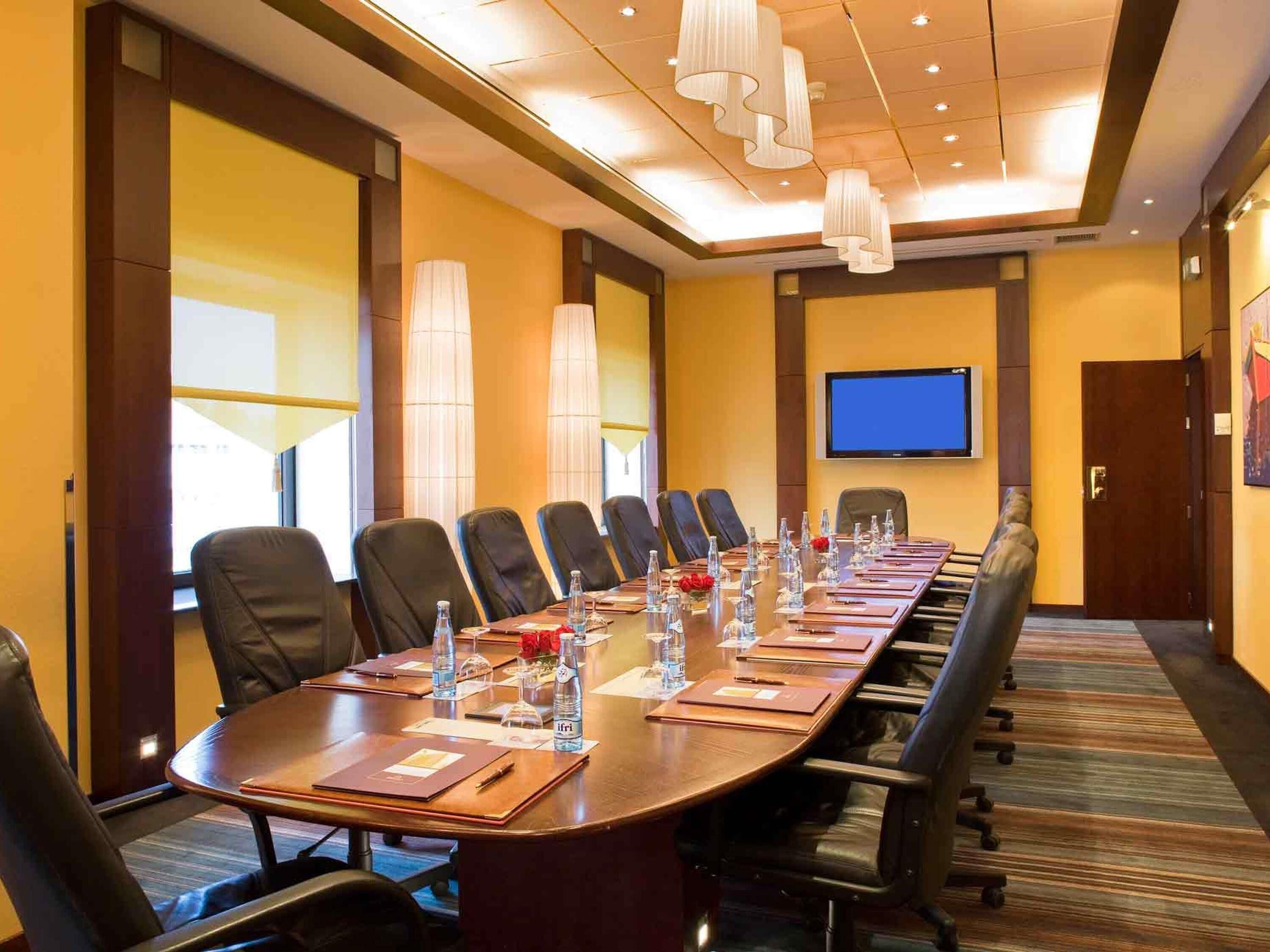 A conference room with a long table, chairs, water bottles, and a TV screen.