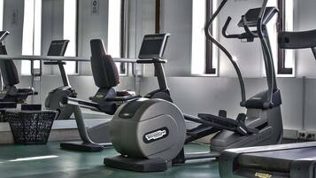 Un gimnasio con diferentes máquinas de ejercicio, una pantalla de televisión y una ventana con persianas.