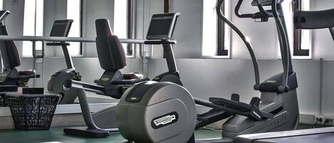 Un gimnasio con diferentes máquinas de ejercicio, una pantalla de televisión y una ventana con persianas.