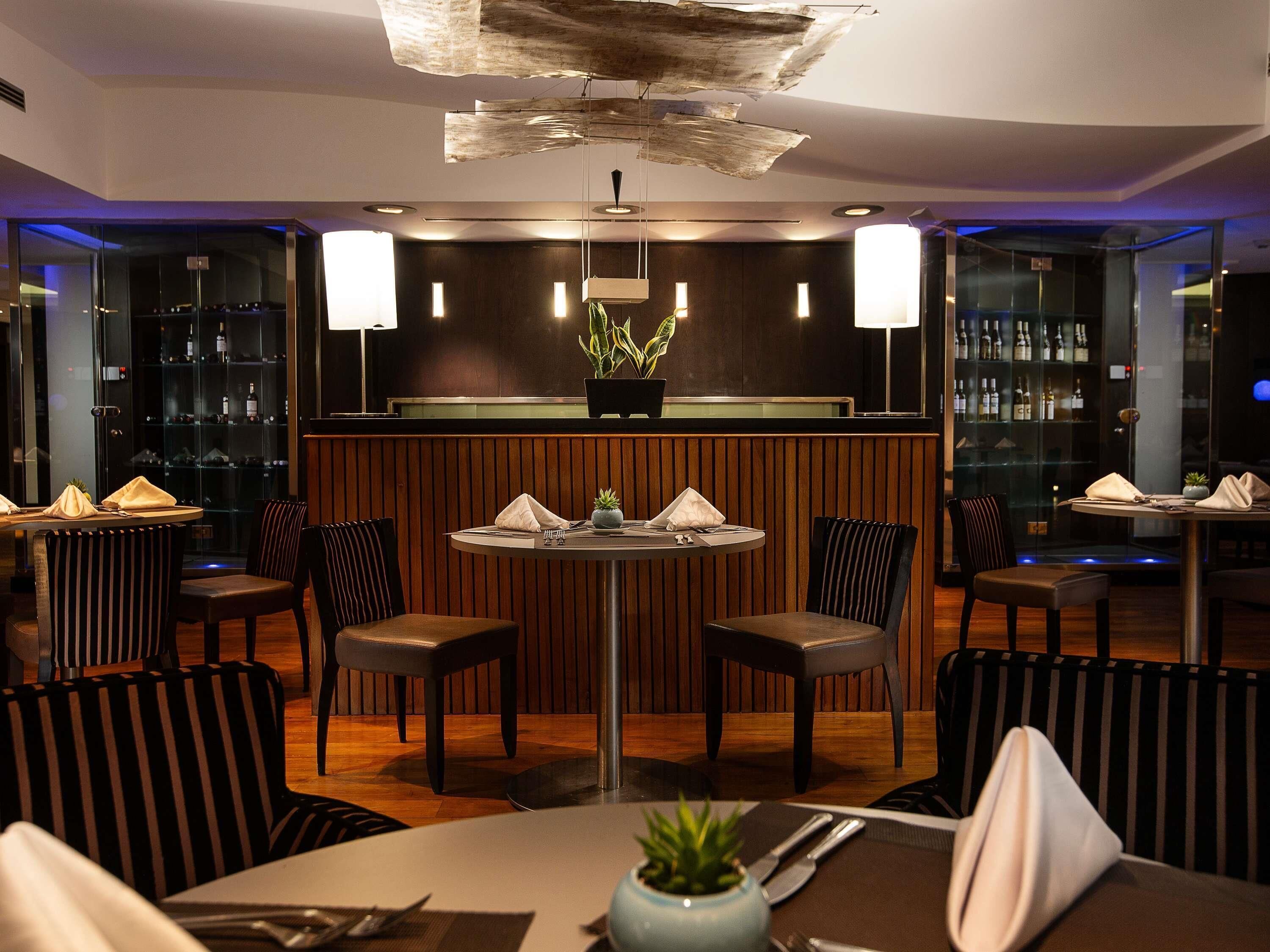 Een restaurant met een ronde centrale tafel, omringd door gestreepte stoelen, en een bar met flessen op de planken.