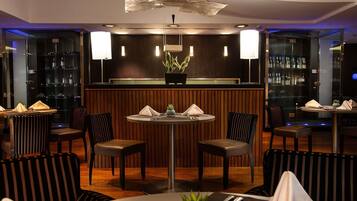 Een restaurant met een ronde centrale tafel, omringd door gestreepte stoelen, en een bar met flessen op de planken.