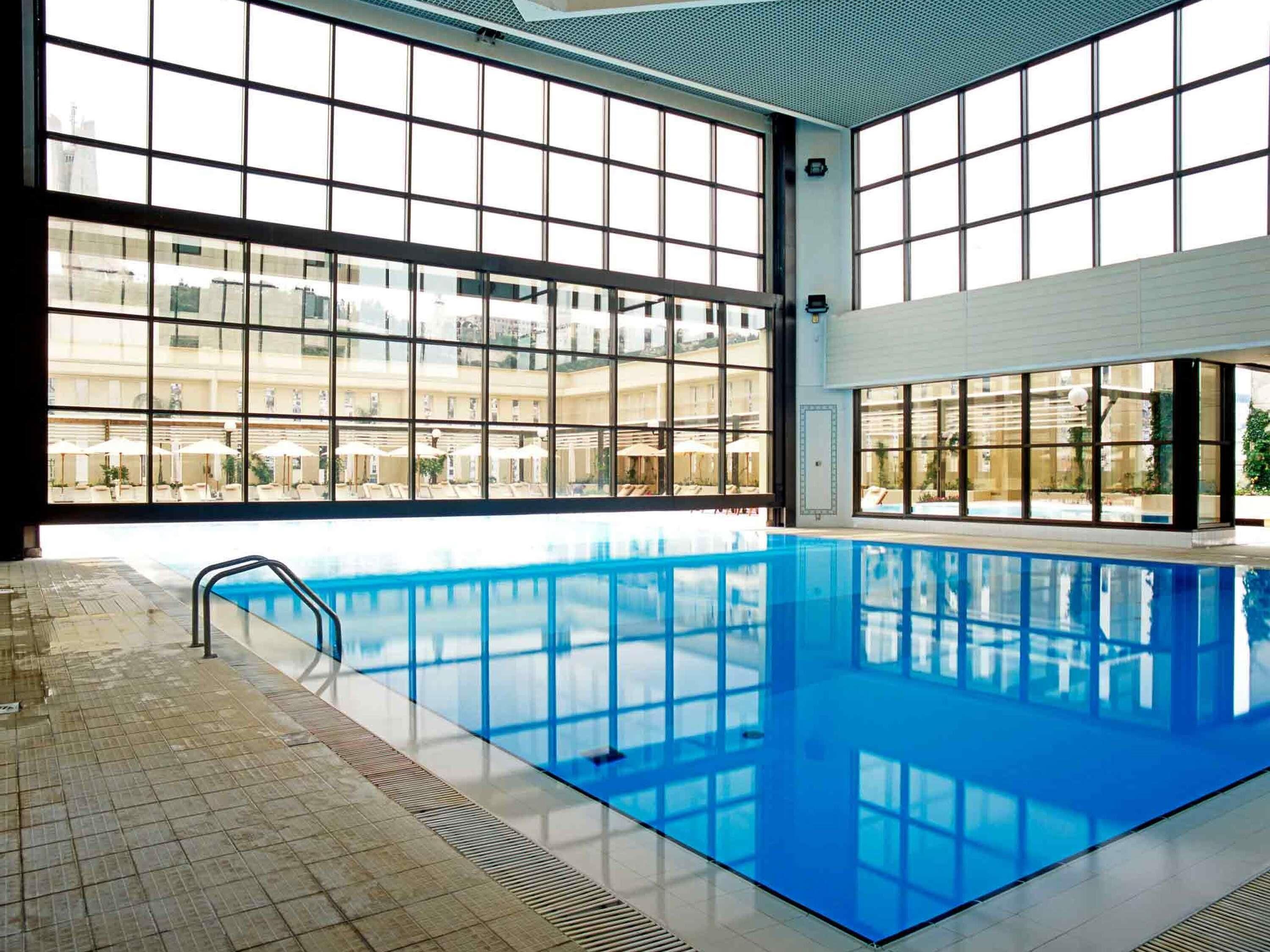 En inomhuspool med stora fönster, kakelgolv och fri utsikt över byggnaderna utanför.