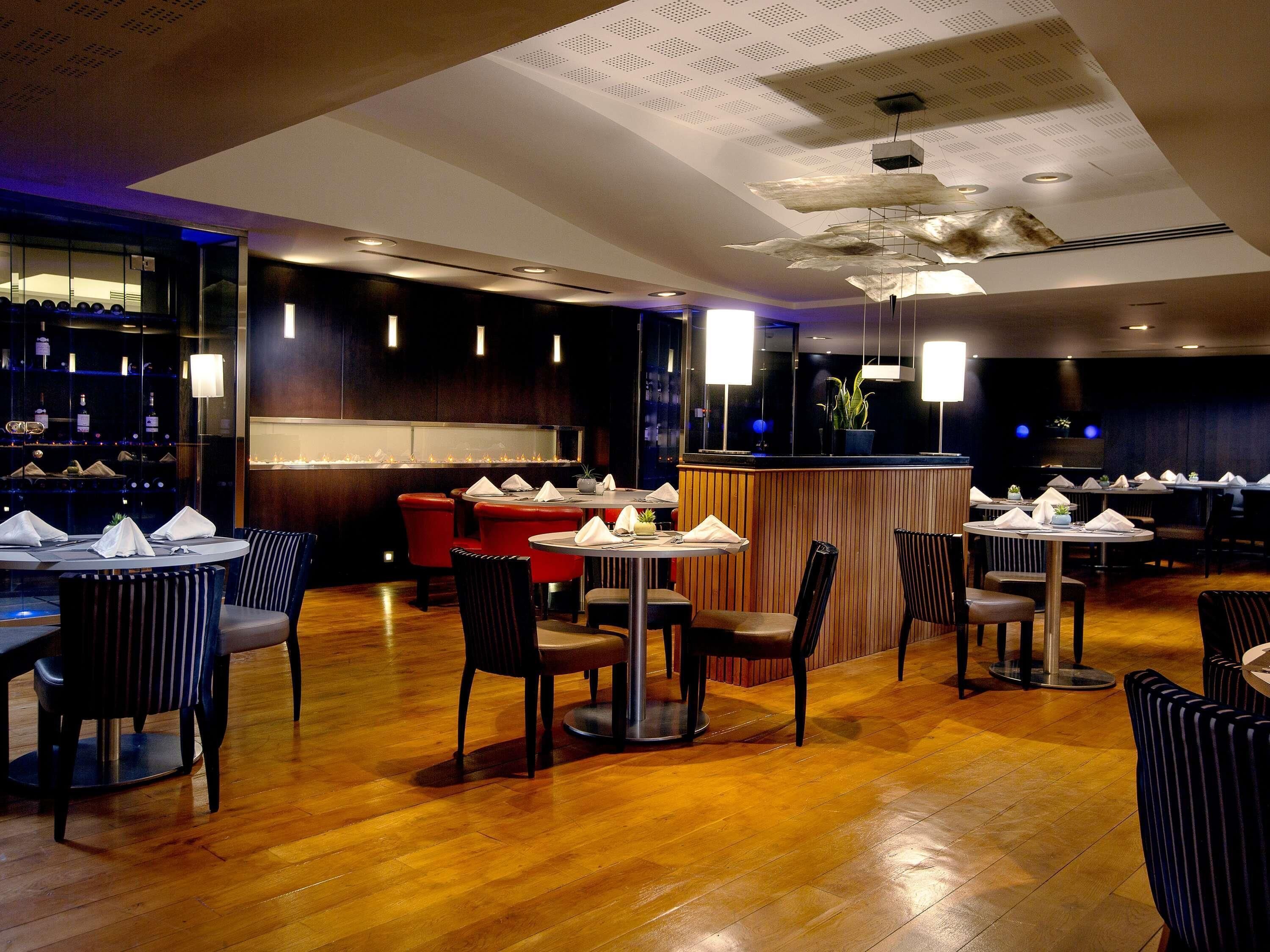 Ein Restaurantinneres mit runden Tischen, roten Stühlen und einer Bar.