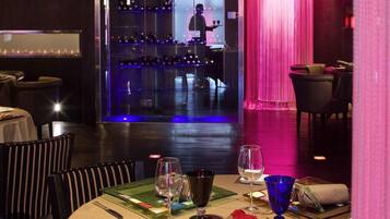 Un restaurante con zona de bar, mesas con copas de vino y un camarero.