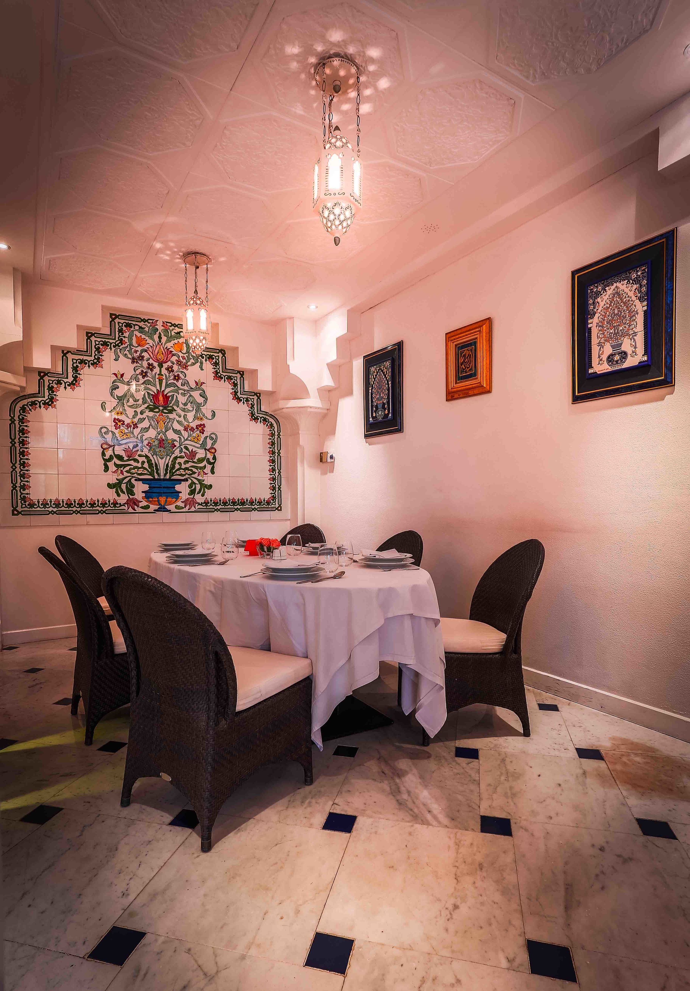 Un comedor con una mesa blanca dispuesta para dos personas, rodeada de sillas de mimbre.
