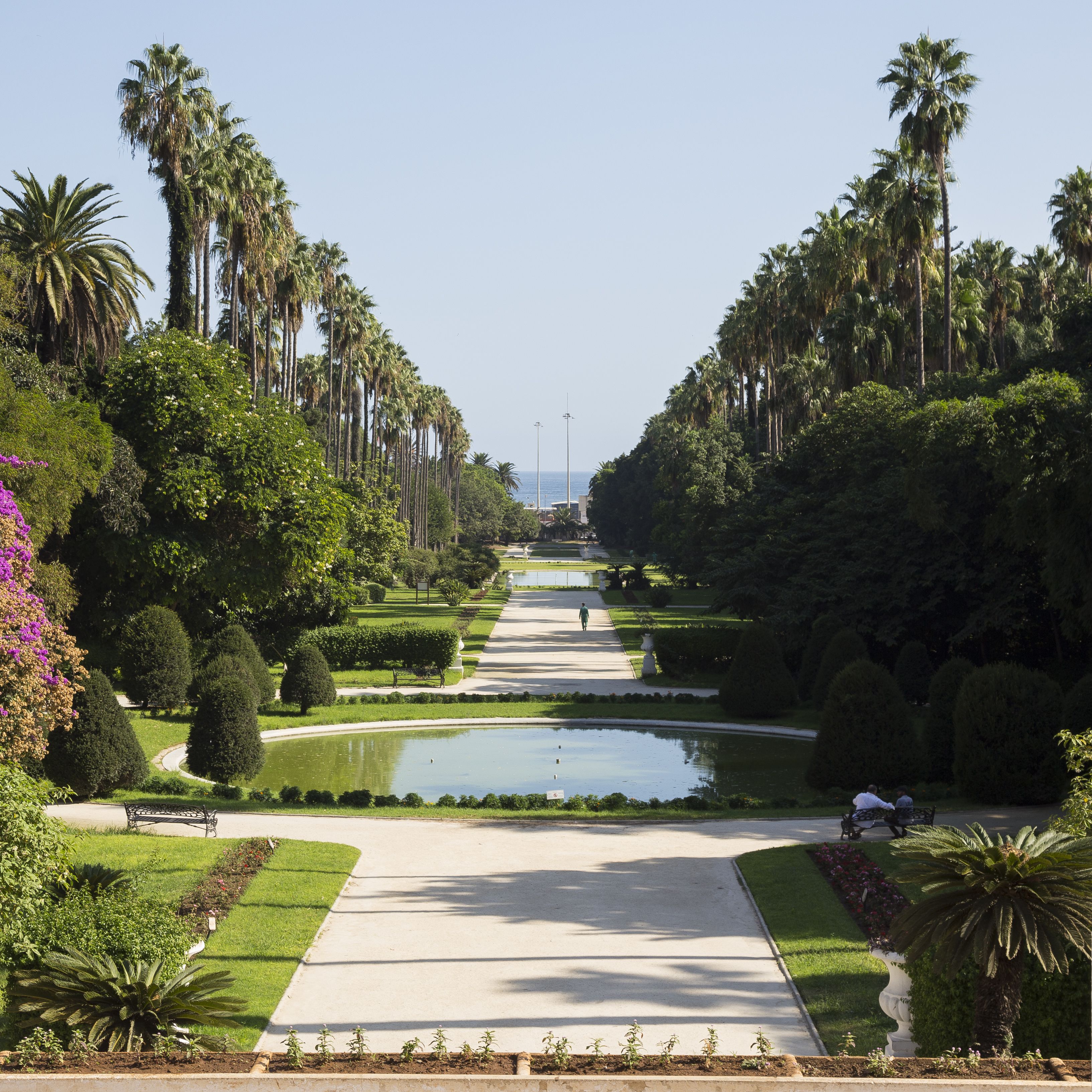 Een formele tuin met een centrale pad, waterpartijen en hoge palmstruiken.
